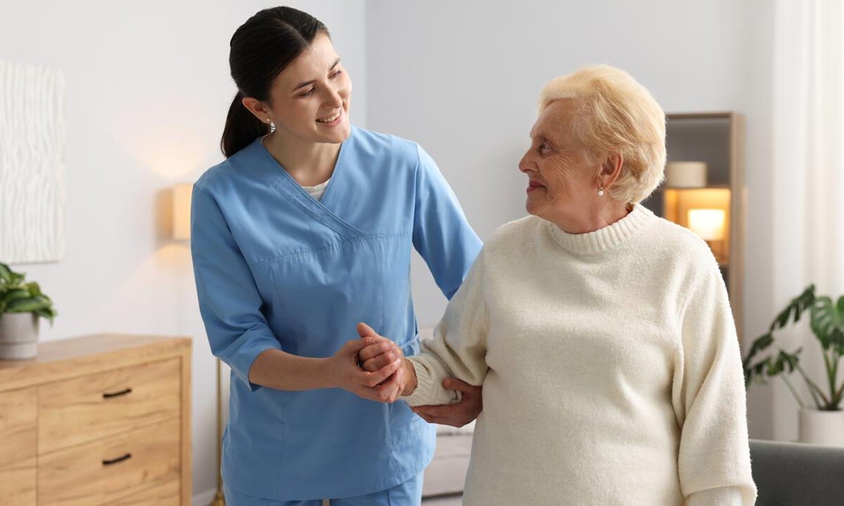 Caregiver steadying an older woman as she stands at home