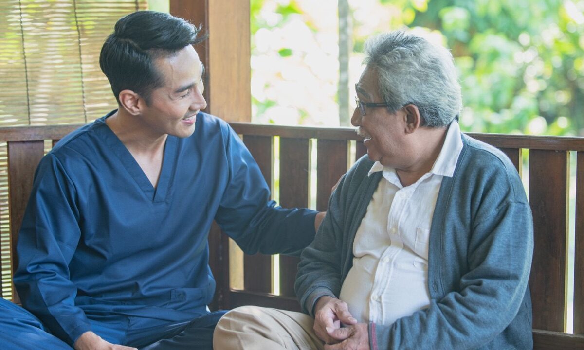 Caregiver and an older man talking together on a shaded porch
