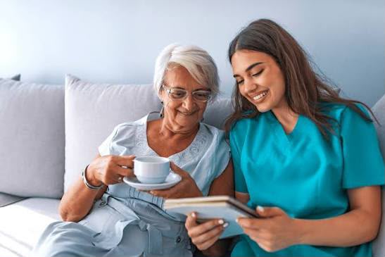 Caregiver and an older woman sitting together on a sofa over a cup of tea