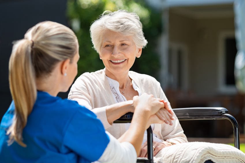 Caregiver holding hands with a smiling older woman outdoors