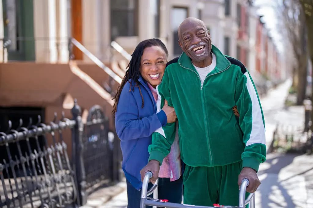 Caregiver walking outdoors with a smiling older man using a walker